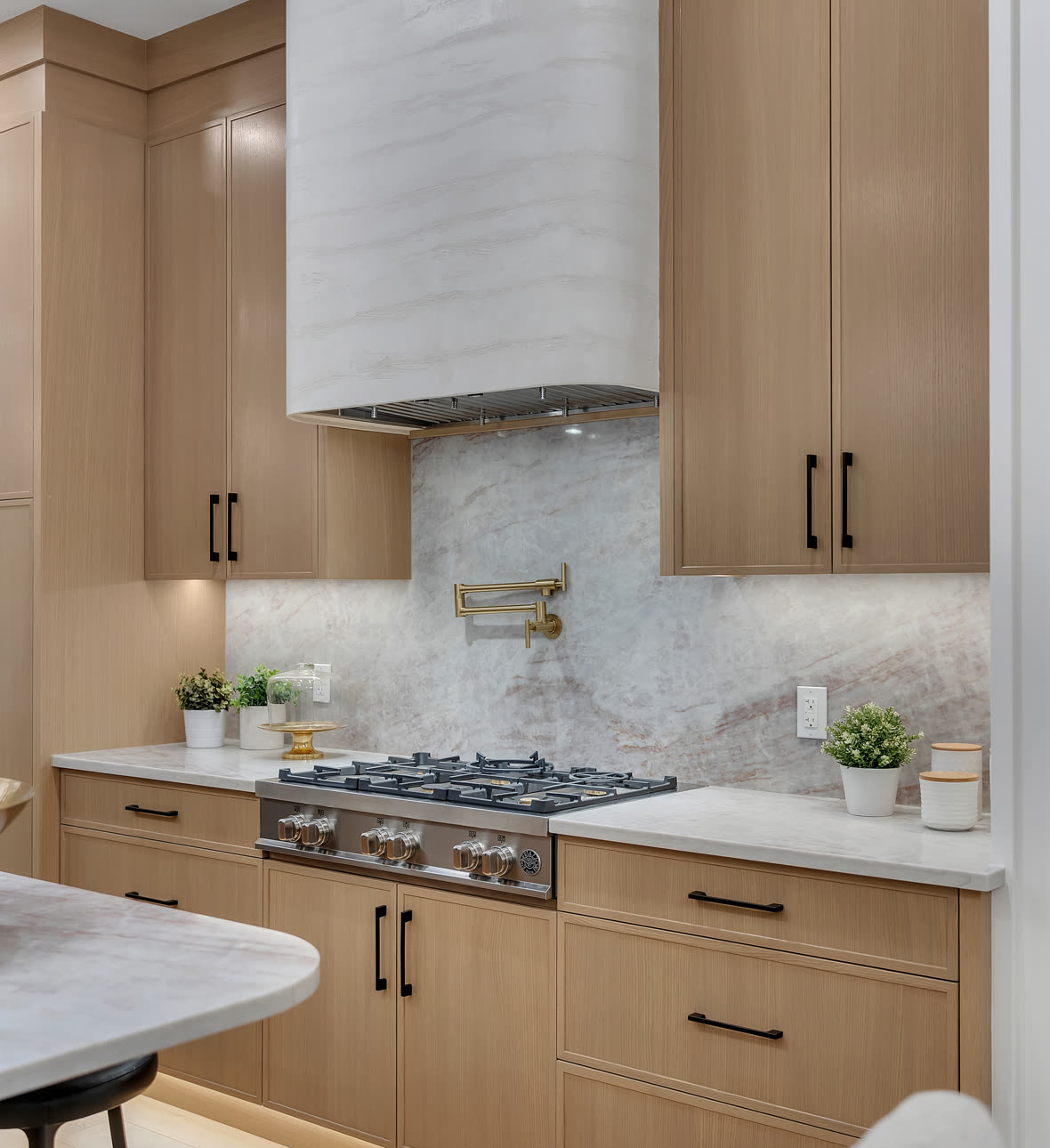 Kitchen with light wood cabinets, a white range hood and a marble backsplash