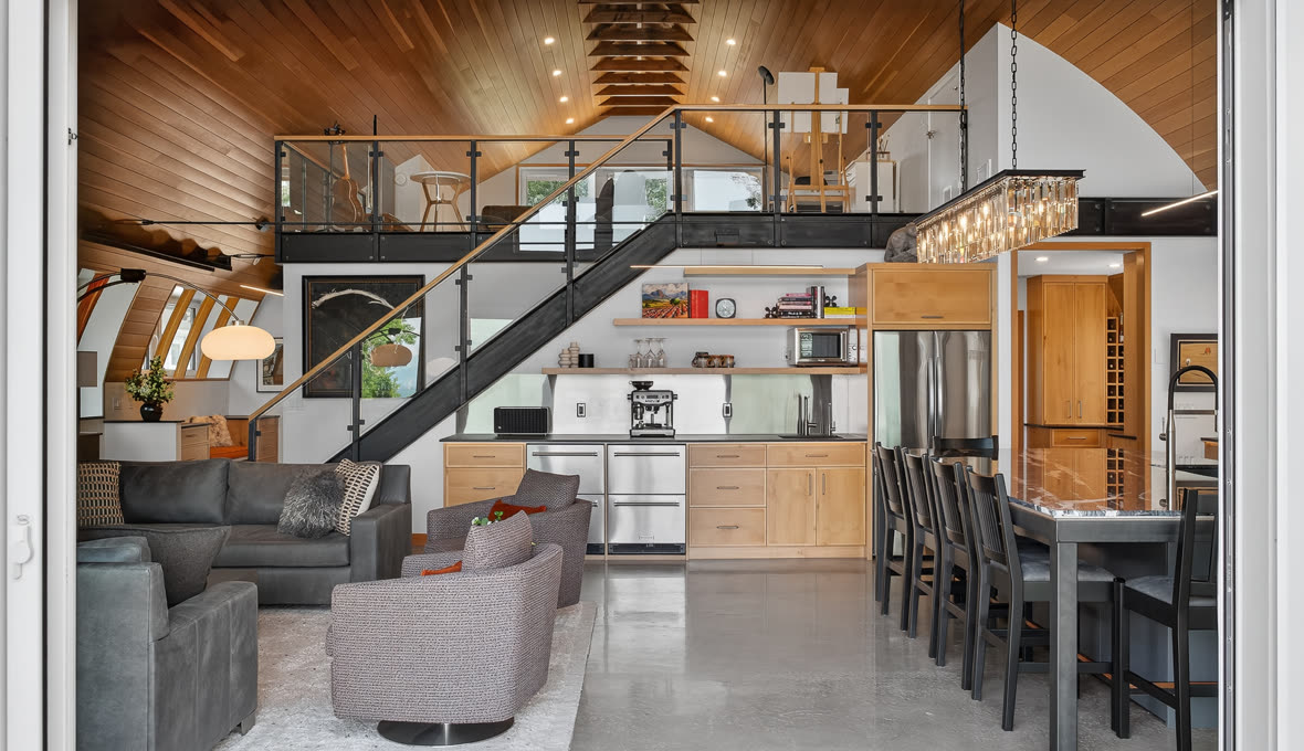 Open-plan main floor with a wood ceiling, steel staircase, living area and kitchen island